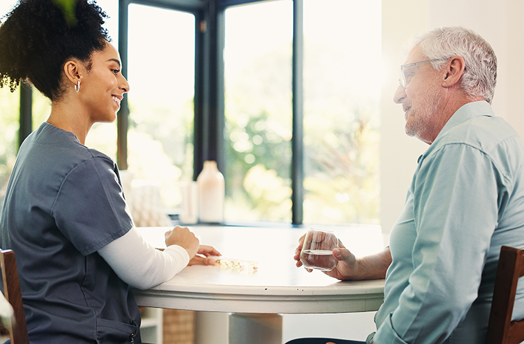 Senior man, nurse and medication with water for healthcare or assisted living in retirement home. Happy caregiver, male person or diagnosis with medical pills for treatment or elderly care in house
