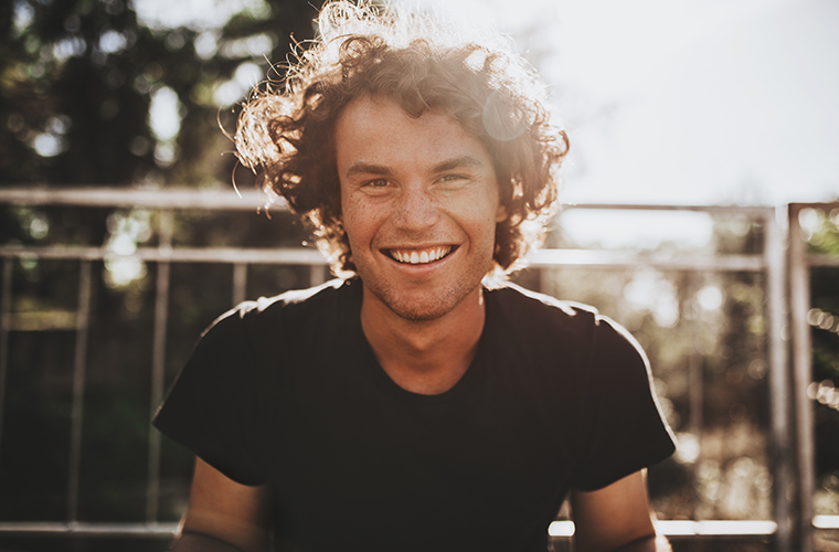 Outdoor closeup portrait of handsome freckled smiling male with curly hair, posing for social advertisement