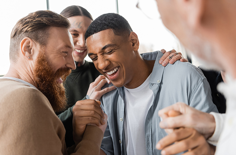Positive people hugging african american man during alcoholics meeting and therapy in rehab center.